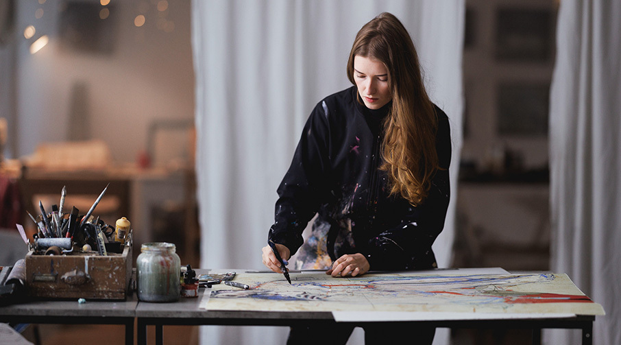Ung kvinne arbeider med å håndkolorere et grafisk trykk i sitt atelier.