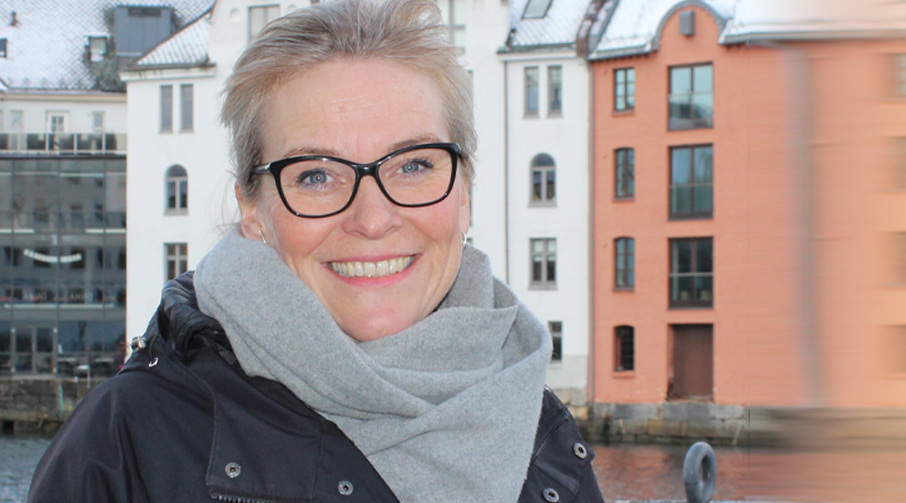 En smilende Lene Trude Solheim, administrerende direktør i Næringsforeningen, foran de fargerike bygningene i Brosundet.